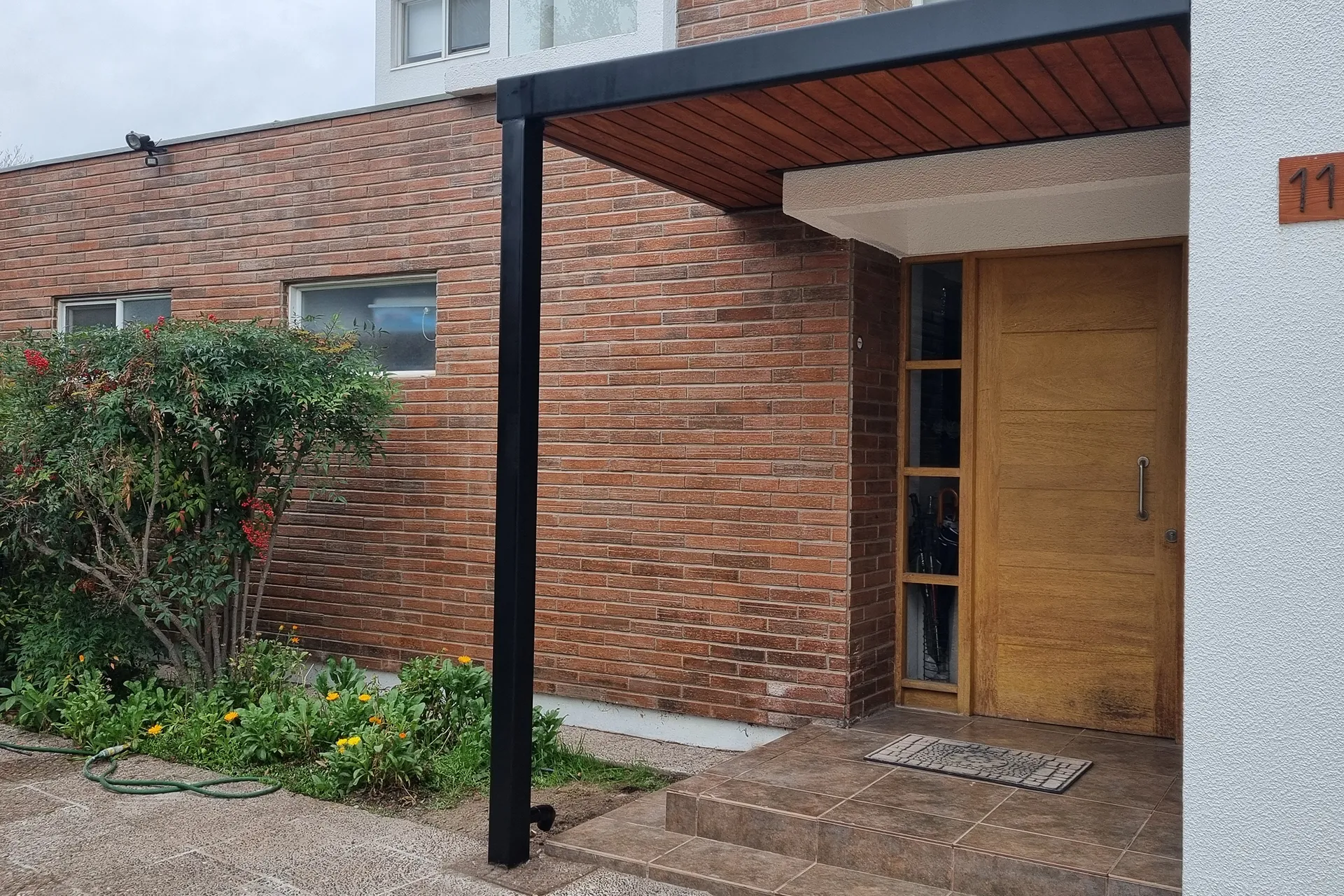 Cobertizo de estructura metálica negra con cielo de madera sobre el acceso, Cobertizo Entrada La Quebrada